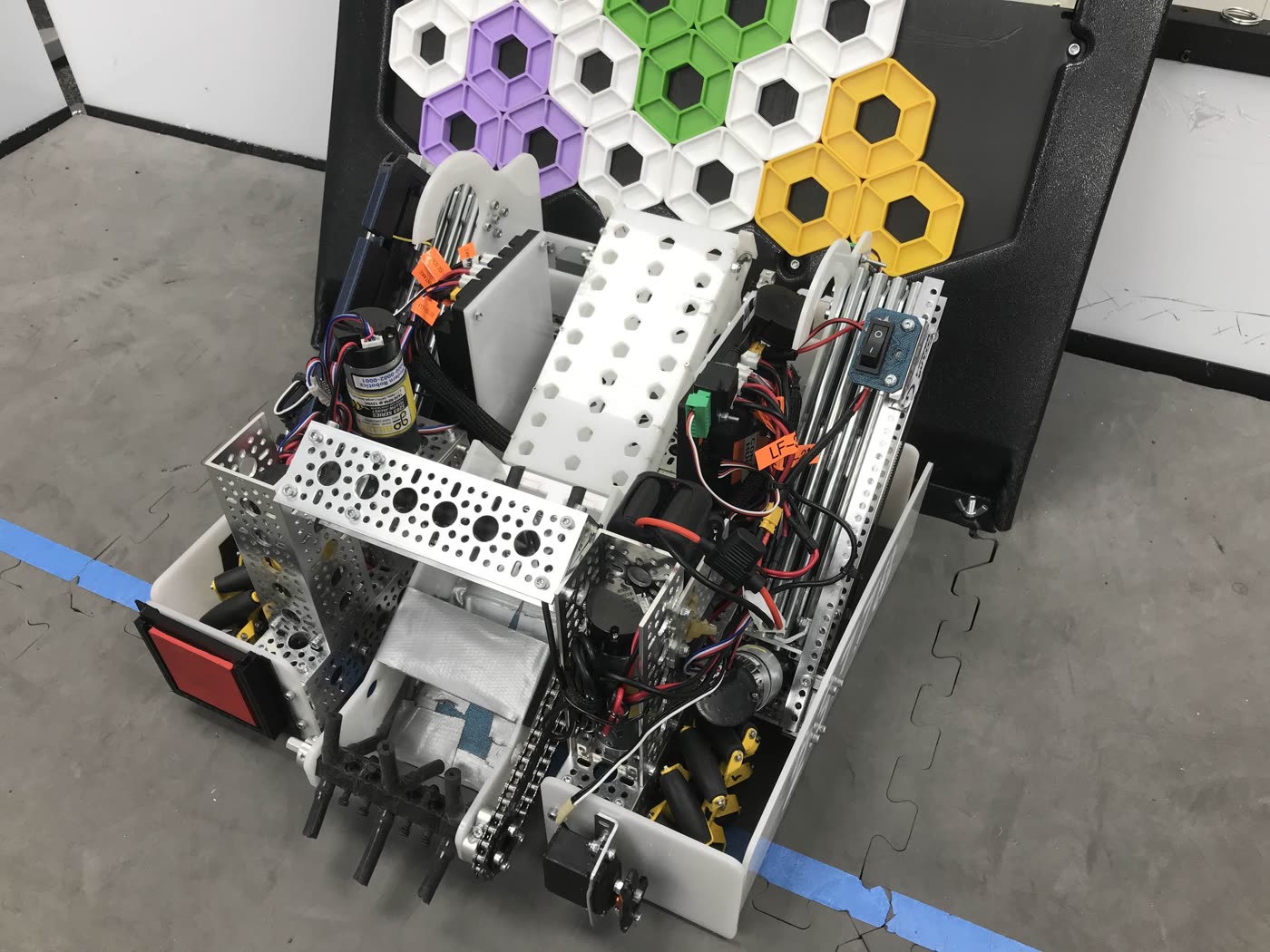 The 23778 robot parked against the backdrop, its white 3D-printed side panels and chain drive open to view, with purple, white, green and yellow pixels already scored on the board above it.