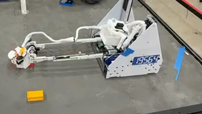 The 19564 robot in the practice space, its horizontal slide extended to the left with the intake claw at the end, and 19564 on a blue plate on the near side.